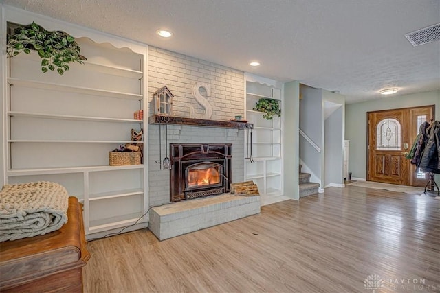 living room with hardwood / wood-style flooring, a fireplace, built in features, and a textured ceiling