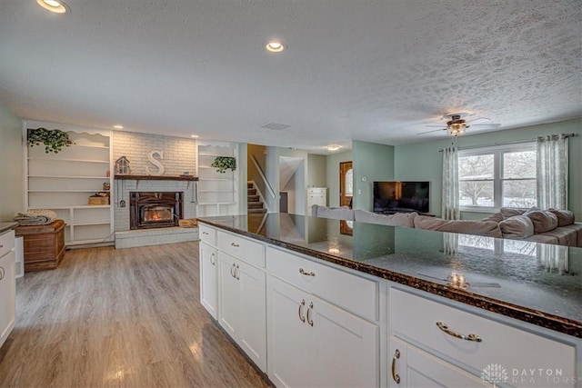 kitchen featuring a fireplace, white cabinets, dark stone counters, a textured ceiling, and light wood-type flooring