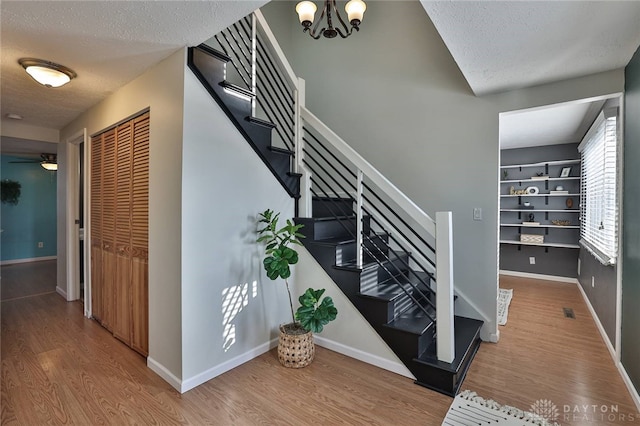 staircase with hardwood / wood-style flooring, ceiling fan with notable chandelier, and a textured ceiling