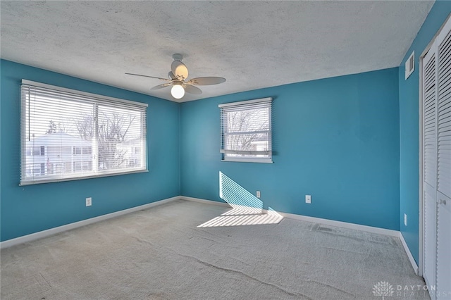 carpeted empty room featuring ceiling fan, a healthy amount of sunlight, and a textured ceiling