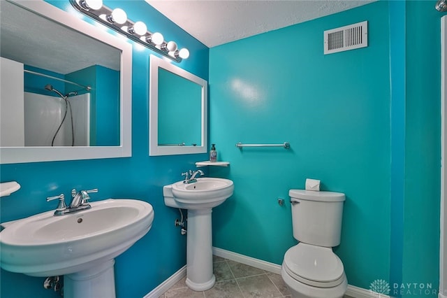 bathroom featuring tile patterned flooring, double sink, walk in shower, toilet, and a textured ceiling