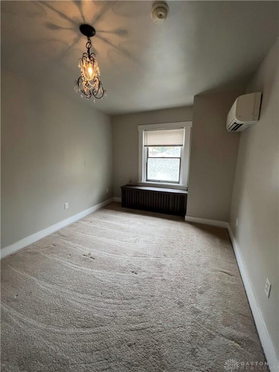 unfurnished room with radiator, an inviting chandelier, a wall unit AC, and carpet flooring