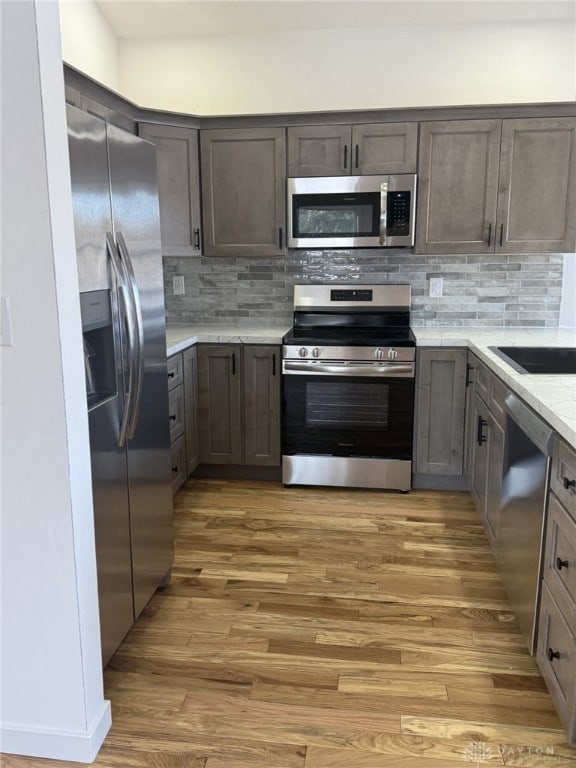 kitchen with appliances with stainless steel finishes, light wood-type flooring, and decorative backsplash