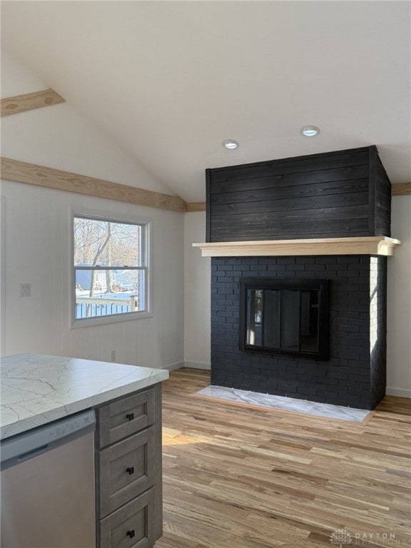 kitchen featuring lofted ceiling, a brick fireplace, light wood-type flooring, stainless steel dishwasher, and light stone countertops