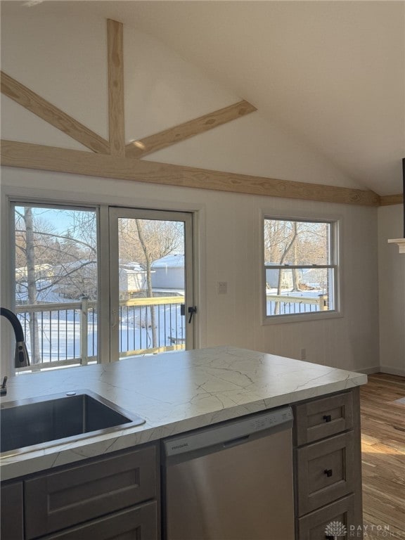 kitchen featuring vaulted ceiling, sink, stainless steel dishwasher, light stone counters, and a water view