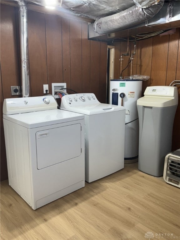 washroom with water heater, separate washer and dryer, light wood-type flooring, and wood walls