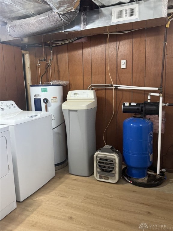 laundry room with wood walls, independent washer and dryer, water heater, and light wood-type flooring