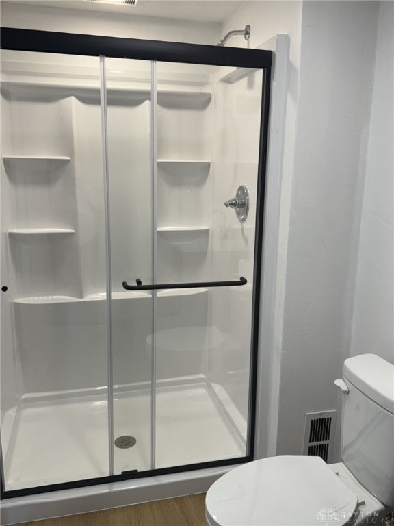 bathroom with hardwood / wood-style floors, an enclosed shower, and toilet