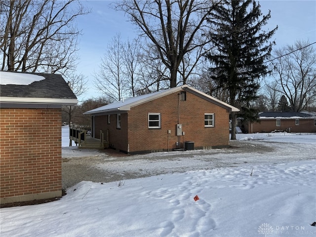 snow covered back of property featuring central AC unit