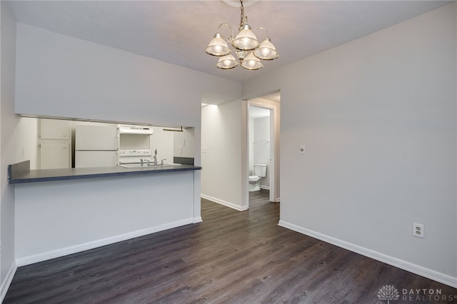 interior space with dark wood-type flooring, kitchen peninsula, hanging light fixtures, and white fridge