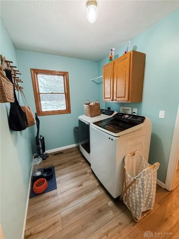 laundry room with cabinets, a textured ceiling, washing machine and clothes dryer, and light hardwood / wood-style floors