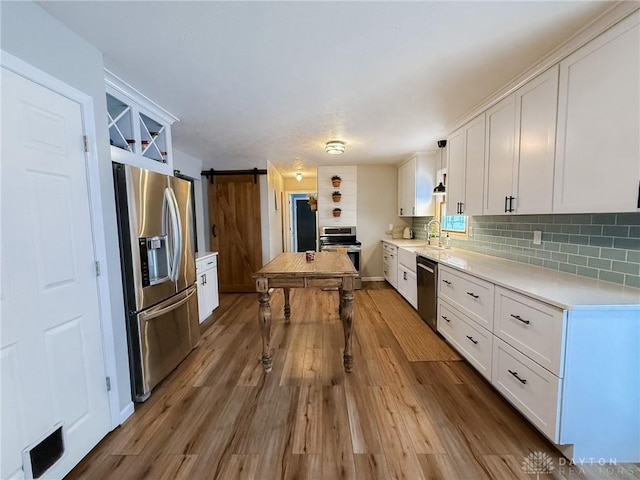 kitchen with sink, white cabinetry, hanging light fixtures, stainless steel appliances, and a barn door