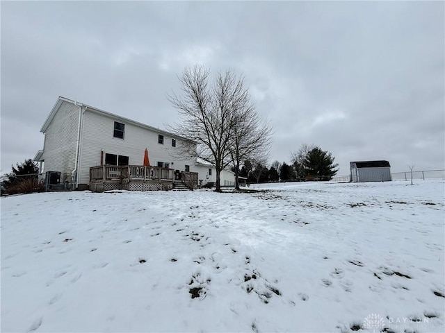 snow covered back of property featuring a deck and a storage unit