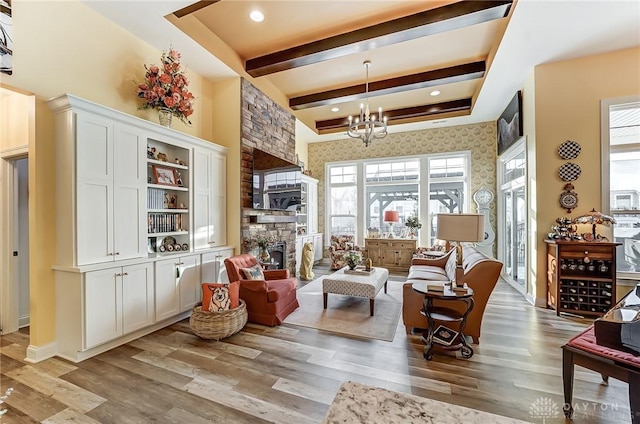 living area with a notable chandelier, a stone fireplace, beam ceiling, and light wood-type flooring