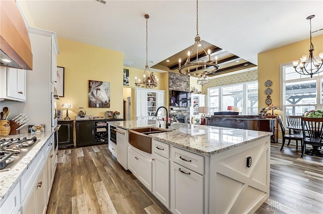 kitchen featuring sink, an inviting chandelier, white cabinetry, an island with sink, and pendant lighting