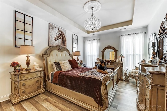 bedroom featuring hardwood / wood-style flooring, a tray ceiling, and a notable chandelier