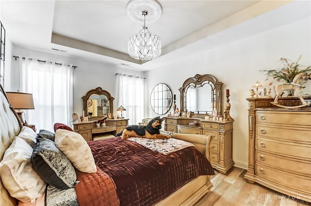 bedroom featuring a notable chandelier, a raised ceiling, and light wood-type flooring