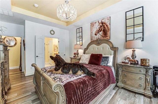 bedroom featuring a tray ceiling, hardwood / wood-style floors, and a notable chandelier