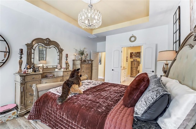 bedroom featuring a raised ceiling, an inviting chandelier, and light hardwood / wood-style flooring