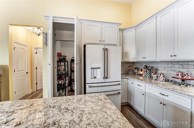 kitchen featuring high end white fridge, white cabinetry, backsplash, dark hardwood / wood-style flooring, and light stone countertops