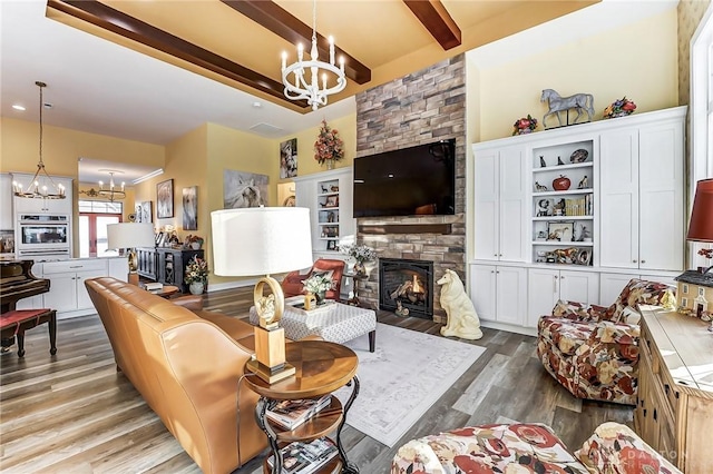 living room featuring beam ceiling, wood-type flooring, a stone fireplace, and an inviting chandelier