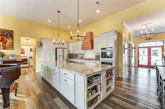 kitchen with white cabinetry, decorative light fixtures, a chandelier, appliances with stainless steel finishes, and a kitchen island with sink