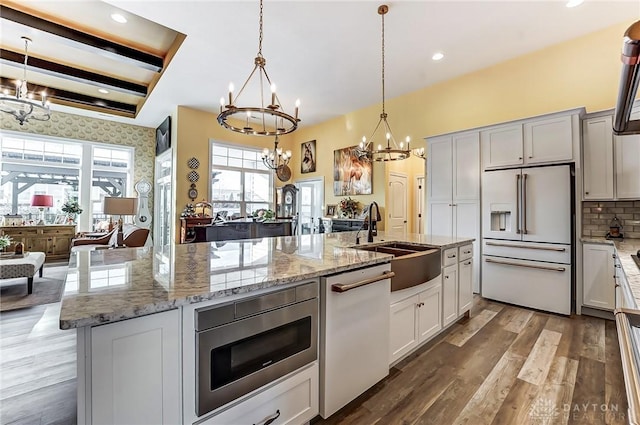 kitchen featuring sink, hanging light fixtures, a kitchen island with sink, white appliances, and an inviting chandelier