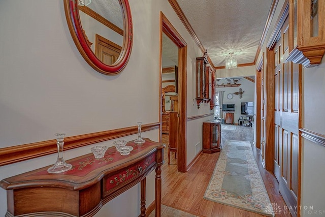 corridor with ornamental molding, light hardwood / wood-style floors, and a textured ceiling