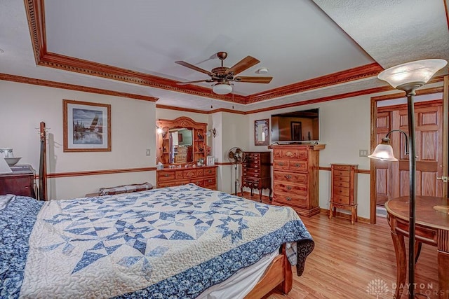 bedroom with ornamental molding, ceiling fan, light hardwood / wood-style floors, and a tray ceiling