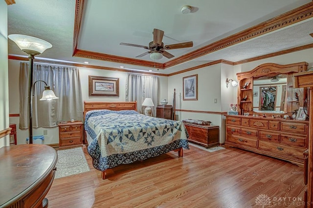 bedroom featuring a tray ceiling, crown molding, light hardwood / wood-style flooring, and ceiling fan