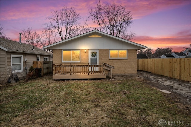 back house at dusk featuring a wooden deck and a yard