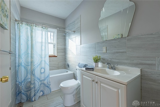 full bathroom with tile walls, vanity, toilet, shower / bathtub combination with curtain, and a textured ceiling