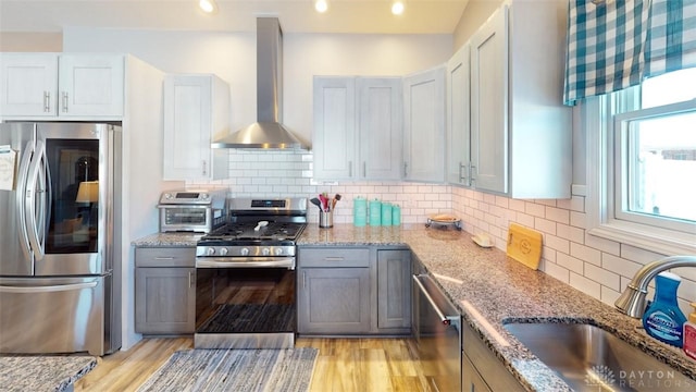 kitchen featuring tasteful backsplash, sink, light stone counters, stainless steel appliances, and wall chimney exhaust hood