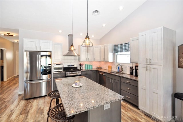 kitchen with pendant lighting, sink, stainless steel appliances, a center island, and light stone countertops