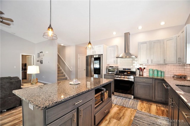 kitchen featuring pendant lighting, white cabinetry, stainless steel appliances, dark stone counters, and wall chimney exhaust hood