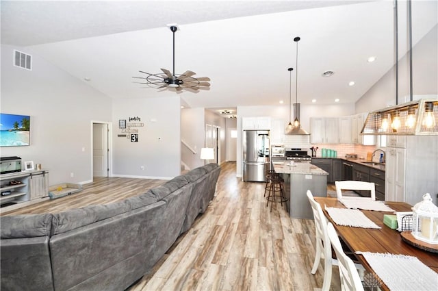 living room featuring ceiling fan, high vaulted ceiling, sink, and light wood-type flooring