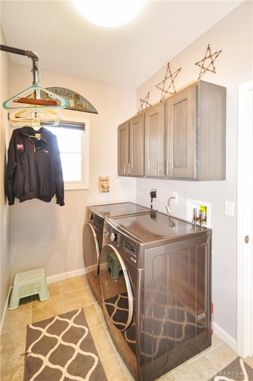 clothes washing area with cabinets, light tile patterned flooring, and washer and clothes dryer