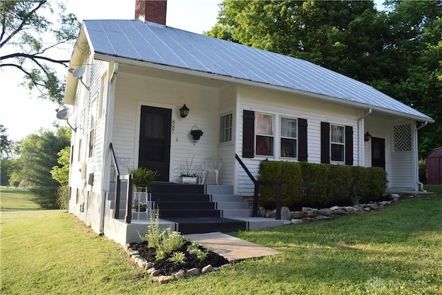 bungalow-style home featuring a chimney, metal roof, and a front yard