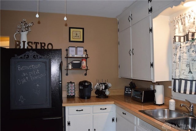 kitchen featuring refrigerator, sink, and white cabinets