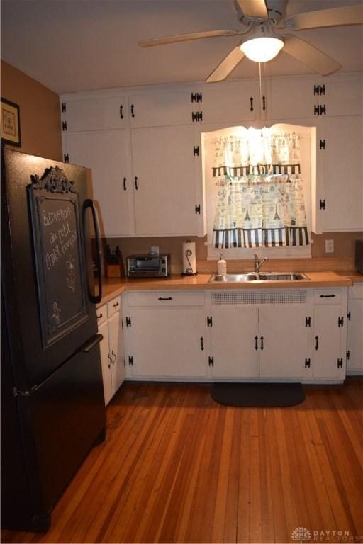 kitchen featuring sink, ceiling fan, black refrigerator, light hardwood / wood-style floors, and white cabinets