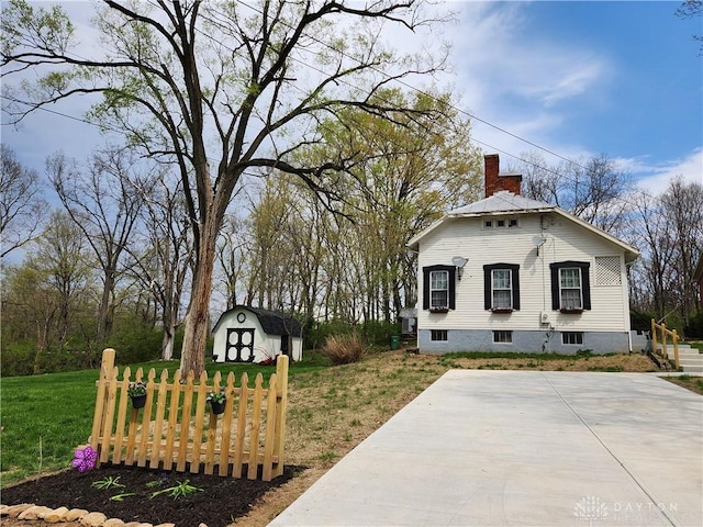 view of front of property featuring a chimney, an outdoor structure, a front lawn, and a storage unit