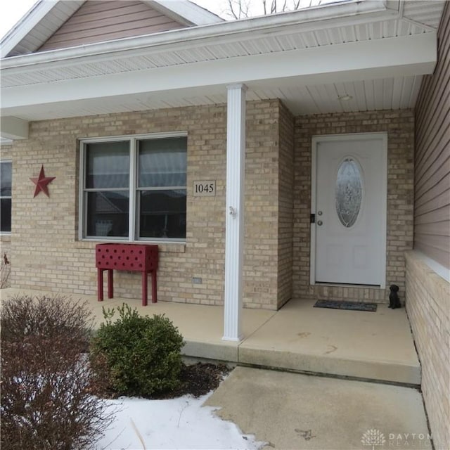 doorway to property featuring covered porch and brick siding