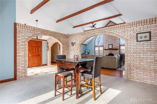 dining room with brick wall, lofted ceiling with beams, and light carpet