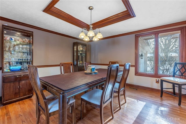 dining space featuring crown molding, an inviting chandelier, light wood-type flooring, and a tray ceiling