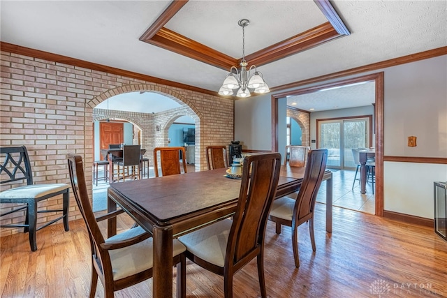 dining room with a notable chandelier, ornamental molding, light hardwood / wood-style floors, brick wall, and a raised ceiling