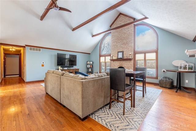 living room with high vaulted ceiling, beamed ceiling, ceiling fan, a fireplace, and light hardwood / wood-style floors