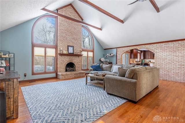 living room with brick wall, high vaulted ceiling, beamed ceiling, light hardwood / wood-style floors, and a brick fireplace