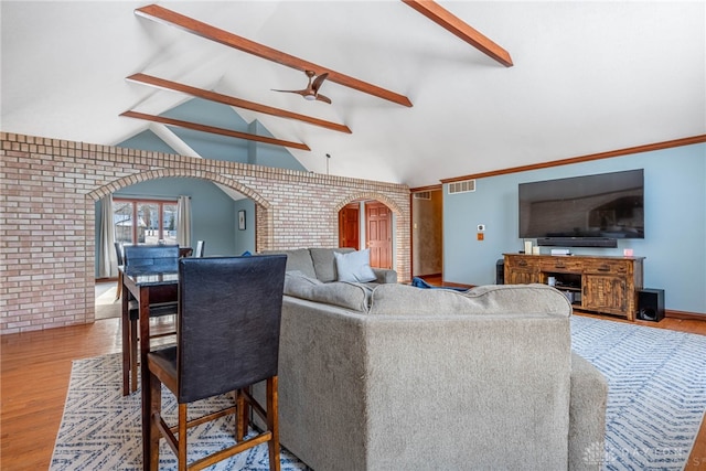 living room with ceiling fan, brick wall, wood-type flooring, and vaulted ceiling with beams