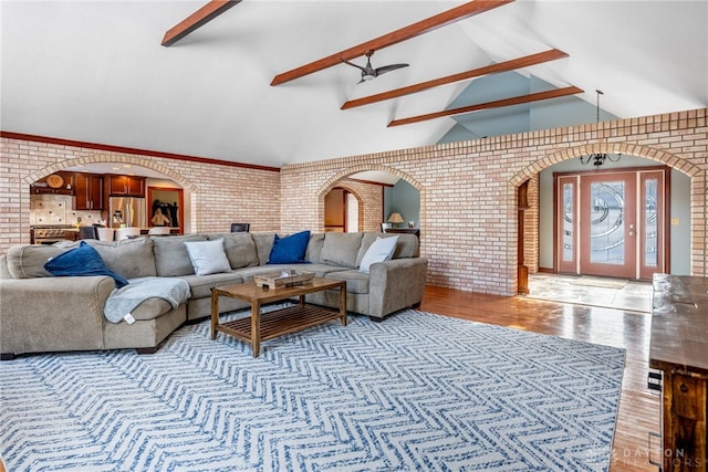 living room with light wood-type flooring, lofted ceiling with beams, ceiling fan, and brick wall