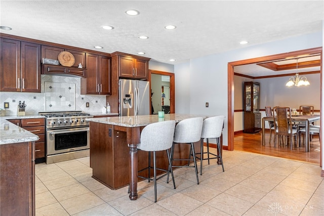 kitchen with hanging light fixtures, stainless steel appliances, a center island, light stone countertops, and decorative backsplash